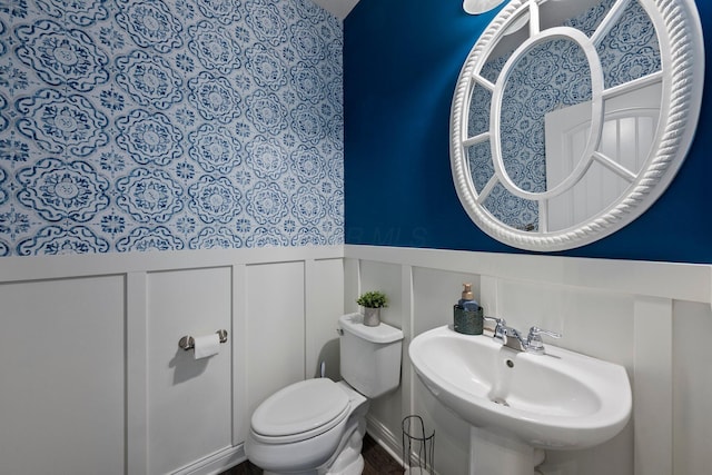 bathroom featuring a sink, a wainscoted wall, a decorative wall, and toilet