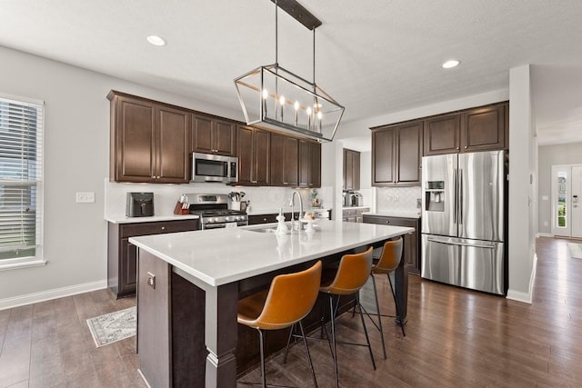 kitchen featuring dark brown cabinetry, appliances with stainless steel finishes, dark wood finished floors, a sink, and light countertops