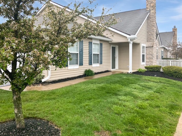view of front of house featuring a chimney, fence, a shingled roof, and a front lawn