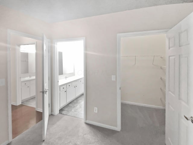 unfurnished bedroom featuring a closet, baseboards, a walk in closet, and light colored carpet