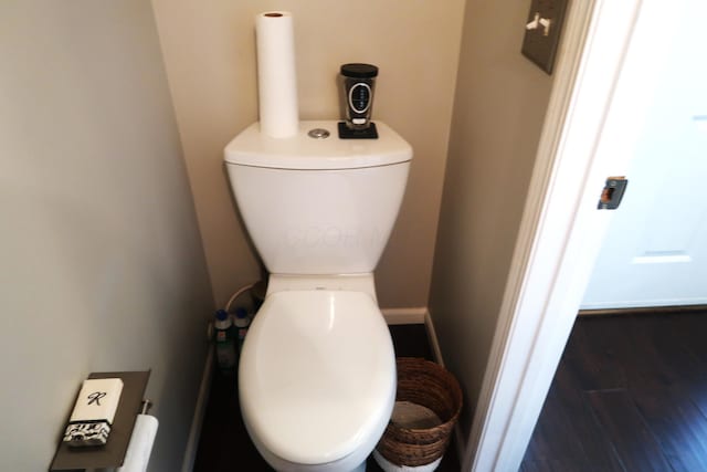 half bath with baseboards, toilet, and wood finished floors