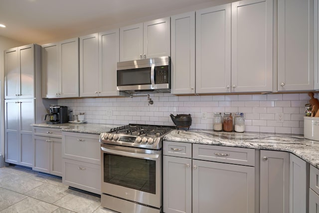 kitchen with appliances with stainless steel finishes, light stone counters, gray cabinets, decorative backsplash, and light tile patterned floors
