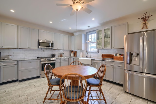 kitchen featuring decorative backsplash, a ceiling fan, appliances with stainless steel finishes, a sink, and gray cabinetry