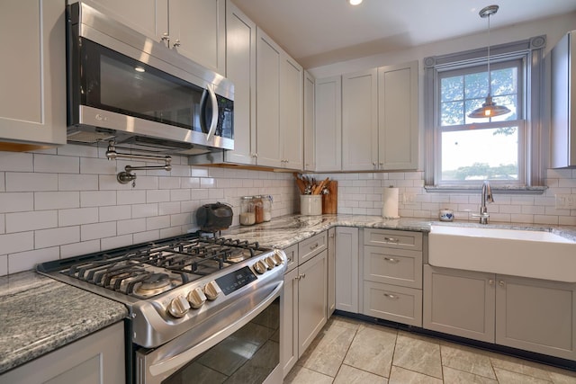 kitchen with light stone counters, a sink, stainless steel appliances, backsplash, and pendant lighting
