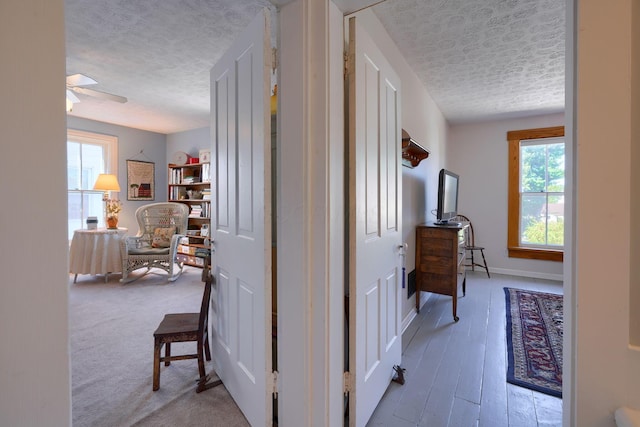 hallway featuring baseboards, a textured ceiling, and a healthy amount of sunlight