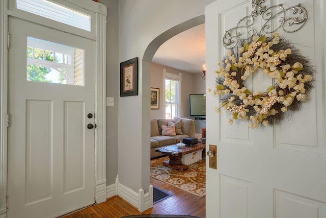 entryway featuring arched walkways, baseboards, and wood finished floors