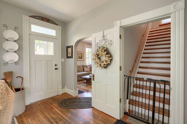 foyer with baseboards, arched walkways, stairs, and wood finished floors