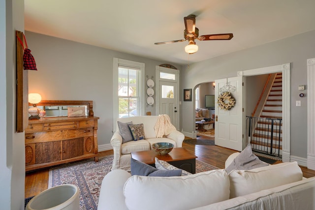living area with ceiling fan, arched walkways, wood finished floors, stairway, and baseboards