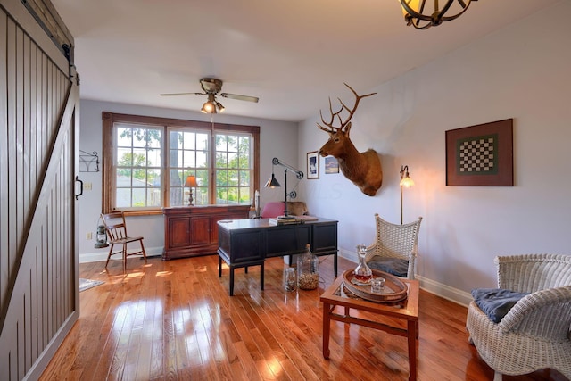 office area with a ceiling fan, baseboards, a barn door, and light wood-type flooring