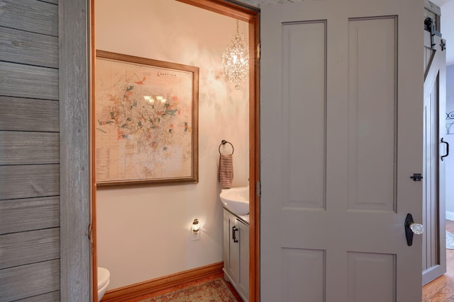bathroom with an inviting chandelier, baseboards, vanity, and toilet