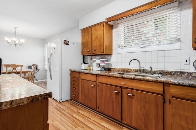 kitchen with brown cabinets, a sink, white refrigerator with ice dispenser, light wood finished floors, and tasteful backsplash