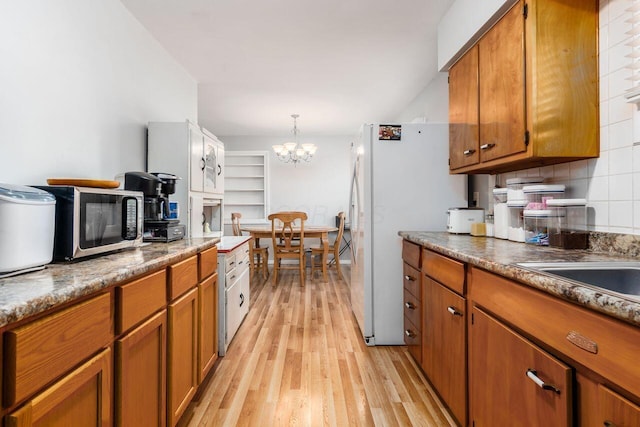 kitchen with brown cabinets, stainless steel microwave, a chandelier, and light wood-type flooring