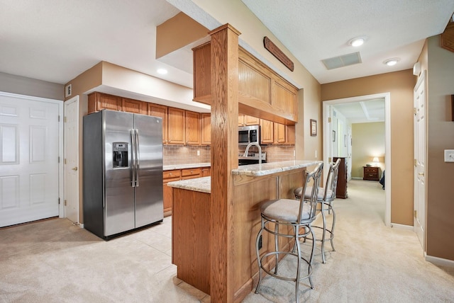kitchen featuring appliances with stainless steel finishes, light carpet, a breakfast bar, and light stone counters