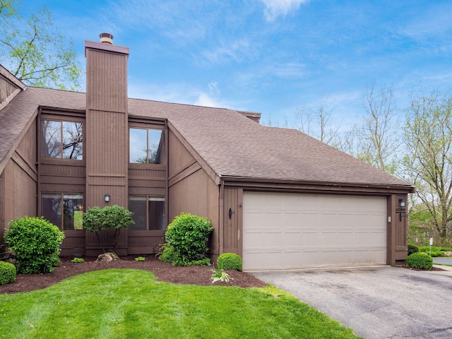 view of front facade featuring a shingled roof, an attached garage, a front yard, a chimney, and driveway