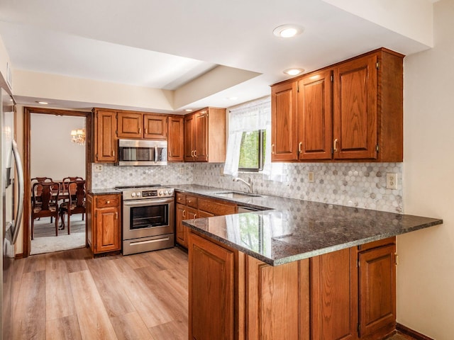 kitchen with brown cabinets, a sink, light wood finished floors, stainless steel appliances, and a peninsula