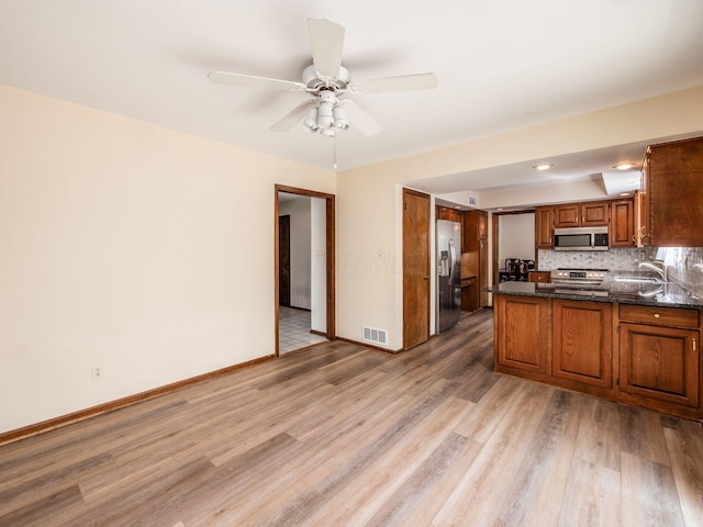 kitchen featuring decorative backsplash, brown cabinetry, visible vents, light wood-style floors, and stainless steel appliances
