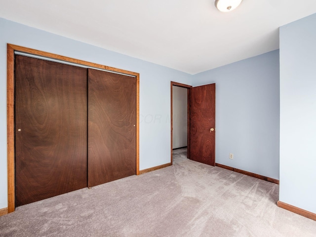 unfurnished bedroom featuring baseboards, a closet, and light colored carpet