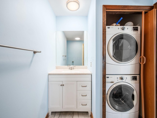 clothes washing area featuring a sink, light wood finished floors, laundry area, and stacked washer and dryer