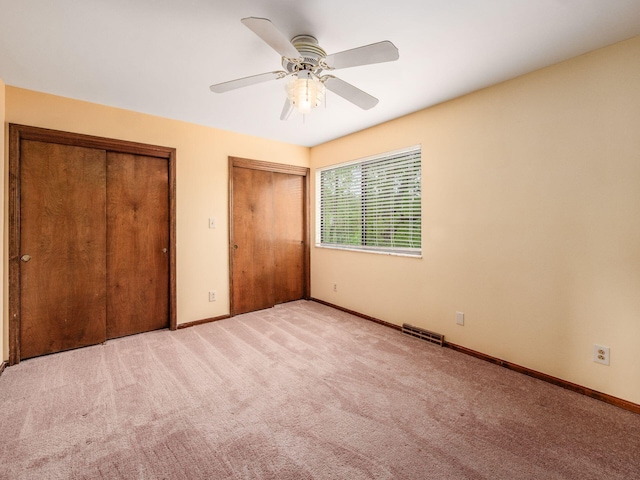 unfurnished bedroom featuring a ceiling fan, visible vents, baseboards, two closets, and carpet flooring