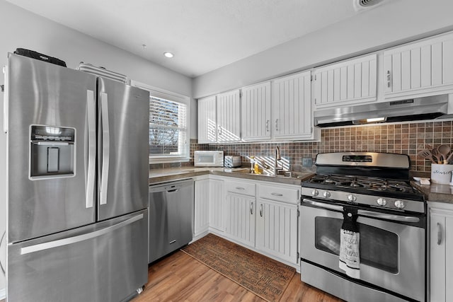 kitchen featuring white cabinets, appliances with stainless steel finishes, a sink, wood finished floors, and under cabinet range hood