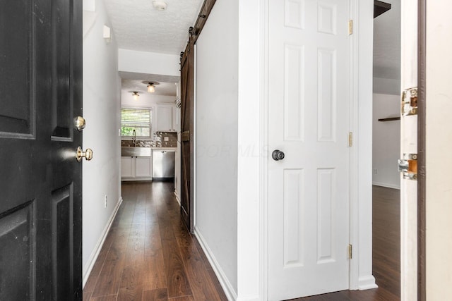 hall featuring a barn door, a sink, a textured ceiling, baseboards, and dark wood-style floors