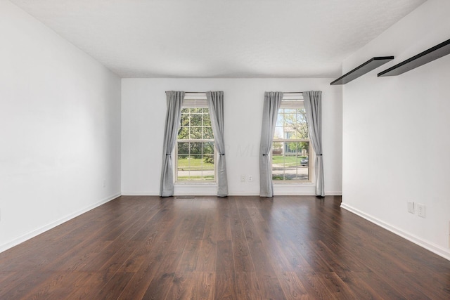 spare room with baseboards and dark wood-type flooring
