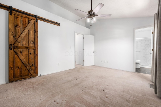 unfurnished bedroom with carpet flooring, visible vents, a barn door, and ensuite bathroom