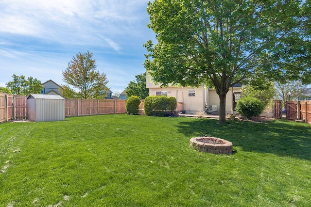 view of yard featuring a storage unit, a fenced backyard, a fire pit, and an outbuilding