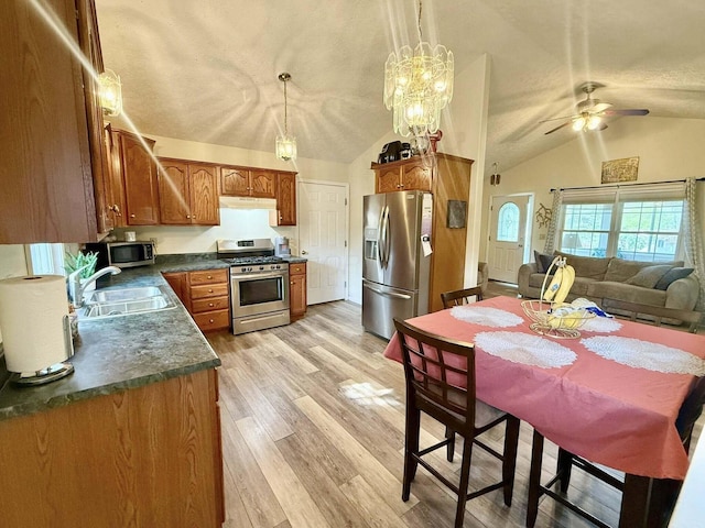 kitchen with appliances with stainless steel finishes, dark countertops, vaulted ceiling, a sink, and under cabinet range hood