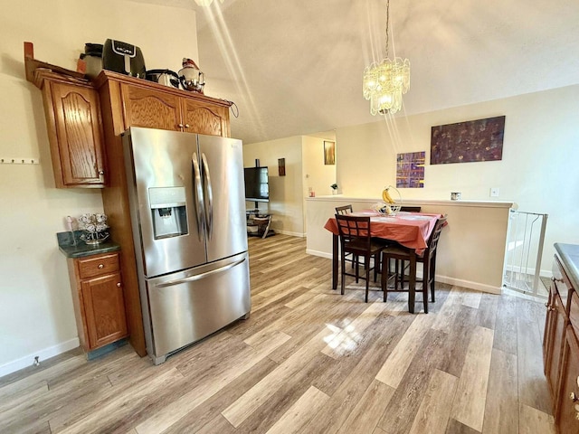 kitchen featuring stainless steel fridge, brown cabinetry, light wood-style flooring, and a notable chandelier