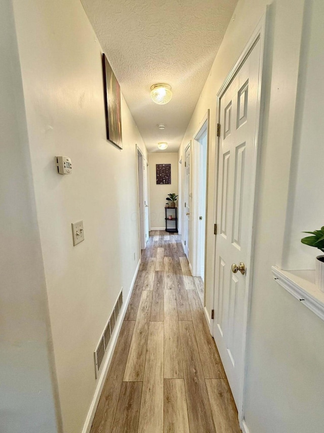 hall featuring a textured ceiling, baseboards, wood finished floors, and visible vents