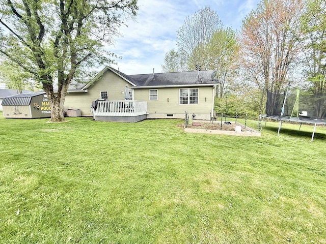 back of property with a trampoline, a storage shed, a wooden deck, an outbuilding, and a lawn