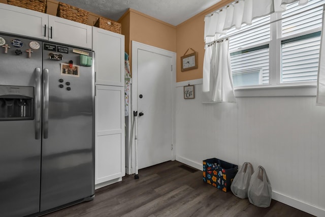 kitchen with stainless steel fridge, white cabinetry, dark wood-type flooring, and baseboards