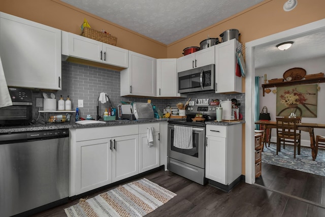 kitchen featuring white cabinets, dark wood-style flooring, a textured ceiling, stainless steel appliances, and decorative backsplash
