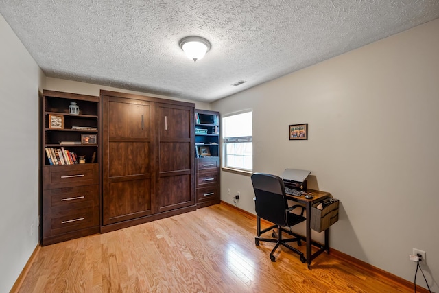 office space featuring a textured ceiling, visible vents, baseboards, and light wood-type flooring