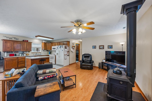 living area featuring baseboards, ceiling fan, a wood stove, and light wood finished floors