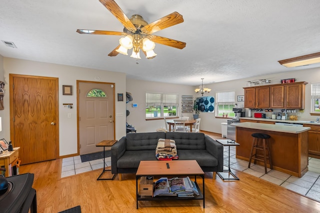 living area with visible vents, a textured ceiling, light wood-style flooring, and ceiling fan with notable chandelier