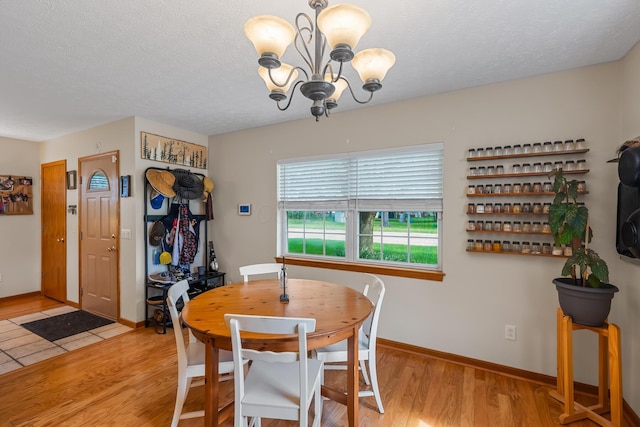 dining space with baseboards, a textured ceiling, light wood finished floors, and a notable chandelier
