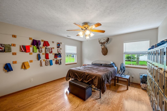 bedroom featuring a textured ceiling, multiple windows, baseboards, and light wood-style floors