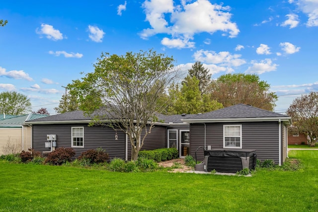back of property featuring a hot tub, a yard, and roof with shingles