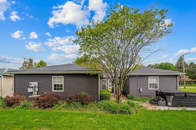 rear view of house featuring a lawn and a hot tub
