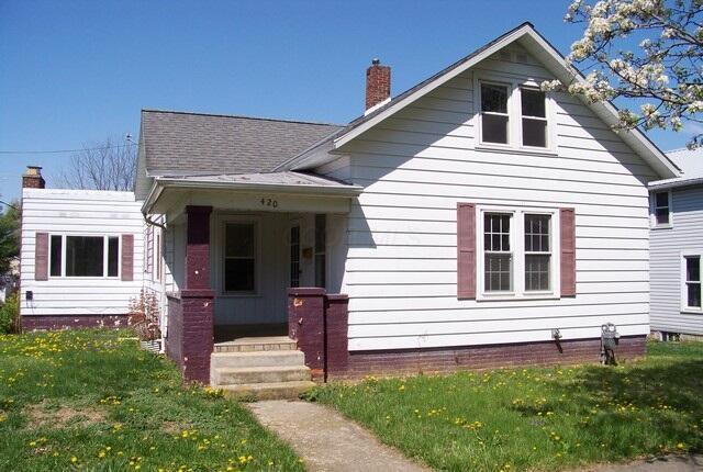 bungalow-style house featuring a front yard, a chimney, and covered porch