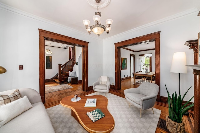 living area with crown molding, an inviting chandelier, wood finished floors, and stairway