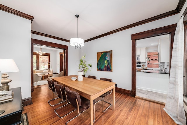 dining space with baseboards, ornamental molding, wood finished floors, and a chandelier