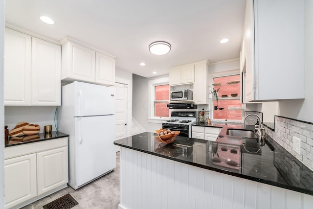 kitchen with a sink, gas stove, freestanding refrigerator, white cabinetry, and stainless steel microwave