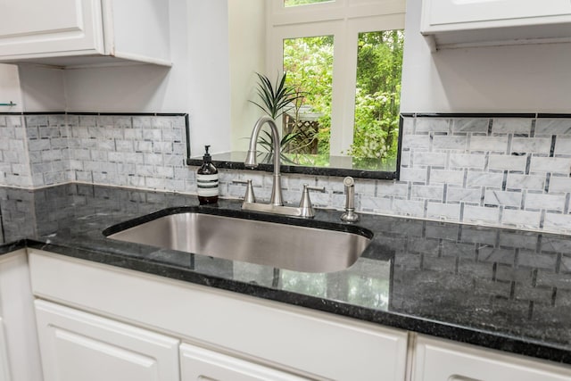 kitchen featuring dark stone counters, white cabinetry, decorative backsplash, and a sink