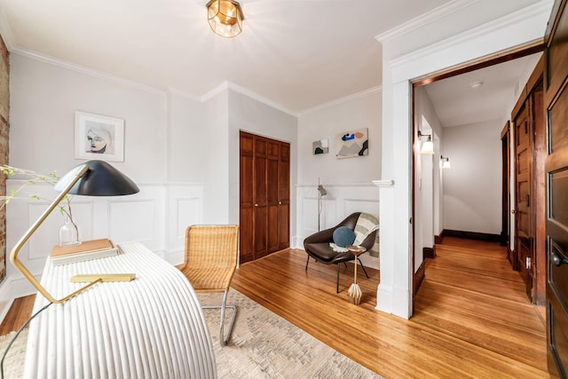 interior space featuring a decorative wall, crown molding, wainscoting, and light wood-type flooring