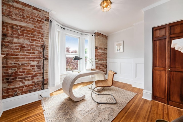 sitting room with brick wall, a wainscoted wall, ornamental molding, and wood finished floors