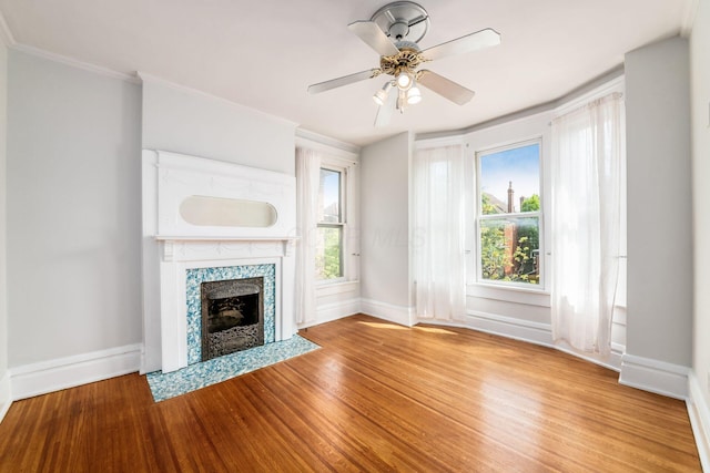 unfurnished living room with baseboards, ornamental molding, wood finished floors, and a tiled fireplace