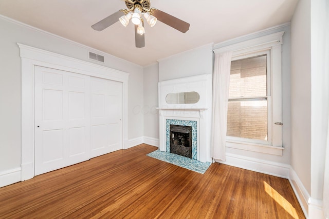 unfurnished living room featuring visible vents, crown molding, wood finished floors, a tile fireplace, and a ceiling fan